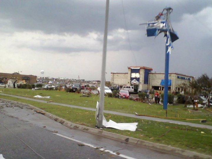 Building with damaged walls still stands behind its mangled sign.
